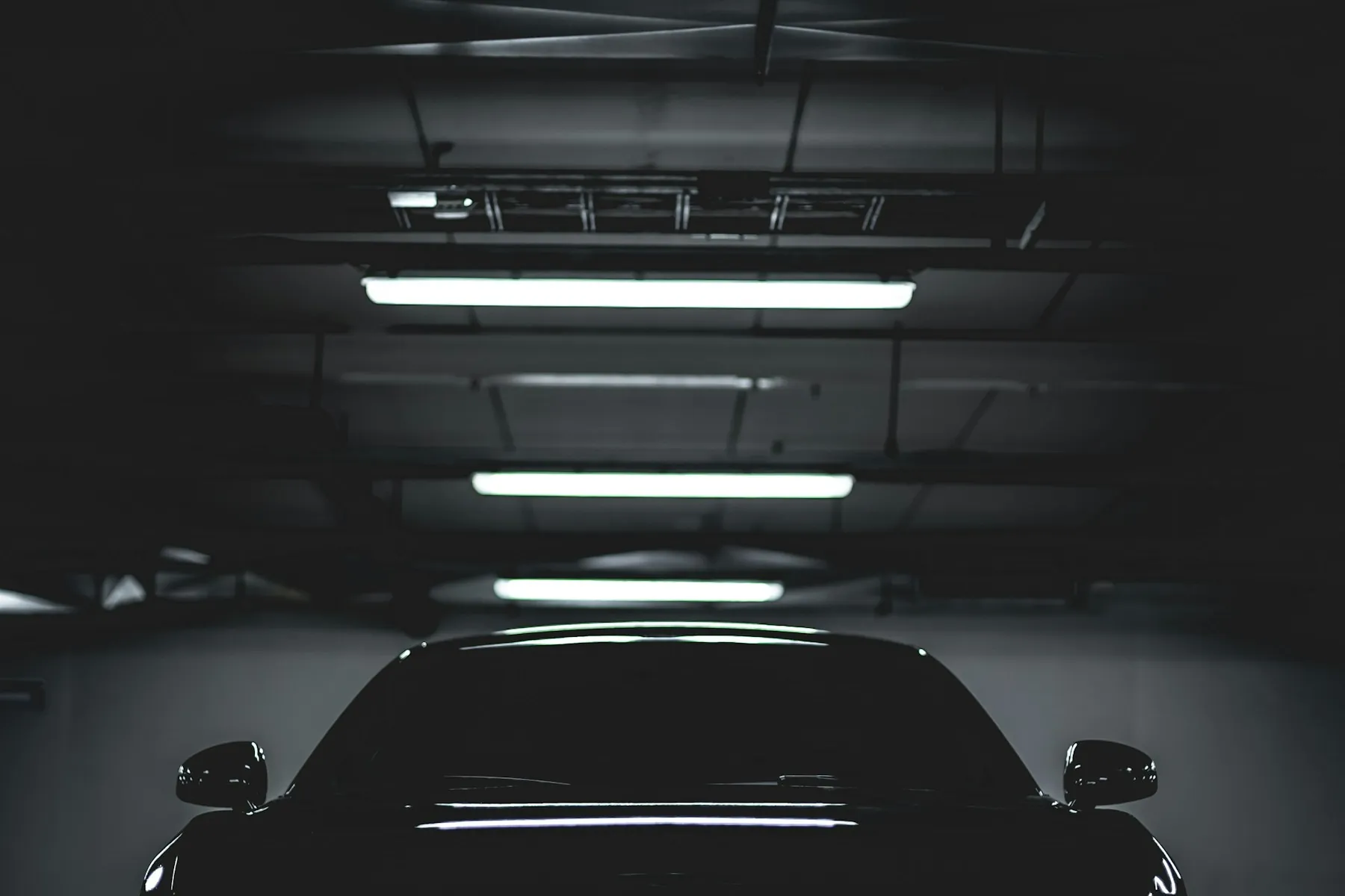 Black car parked in a dark garage under strip lighting